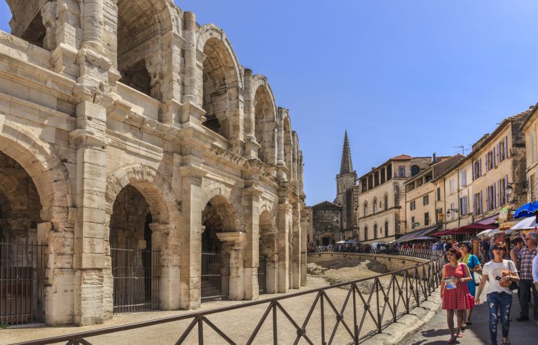 Arles, France - June 6, 2014: Tourists strolling in the old town of Arles, next to the Roman Amphitheatre, one of the main sights of the city. Built in about 80 AD, the amphitheatre was capable of seating over 20,000 spectators, which attended the bloody hand-to-hand combats typical of that period.